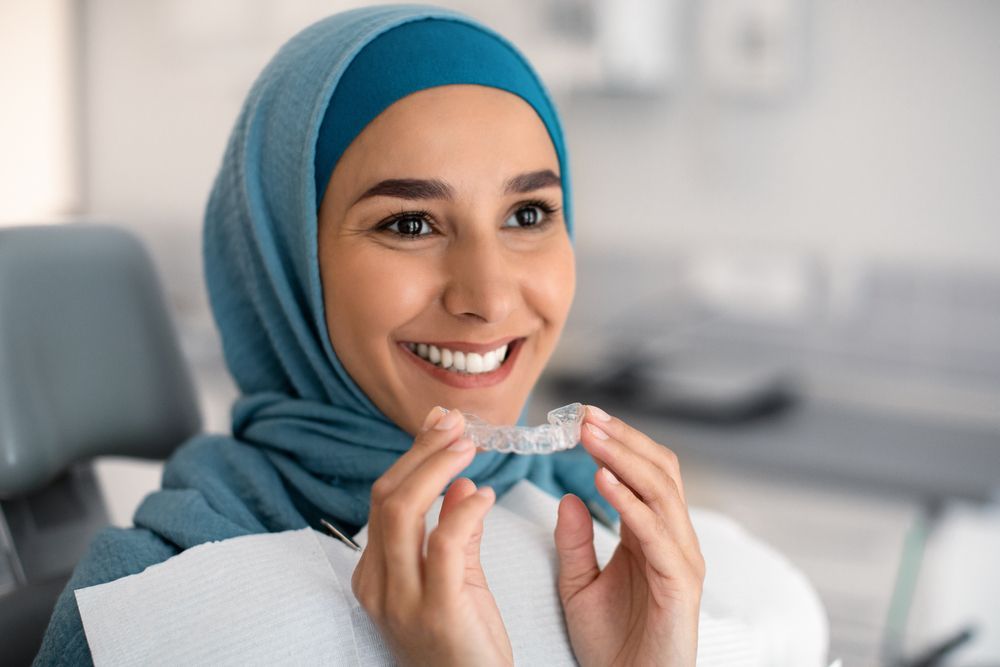 A woman in a hijab is smiling while holding a clear braces.