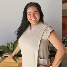A woman in a beige dress is smiling with her hands on her hips