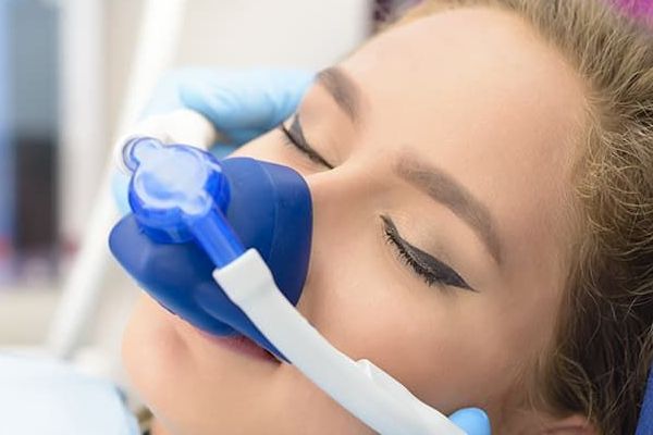 A woman is laying in a dental chair with an oxygen mask on her face.