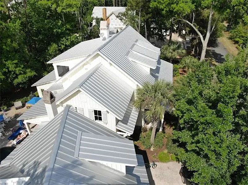 An aerial view of a large white house with a metal roof surrounded by trees.