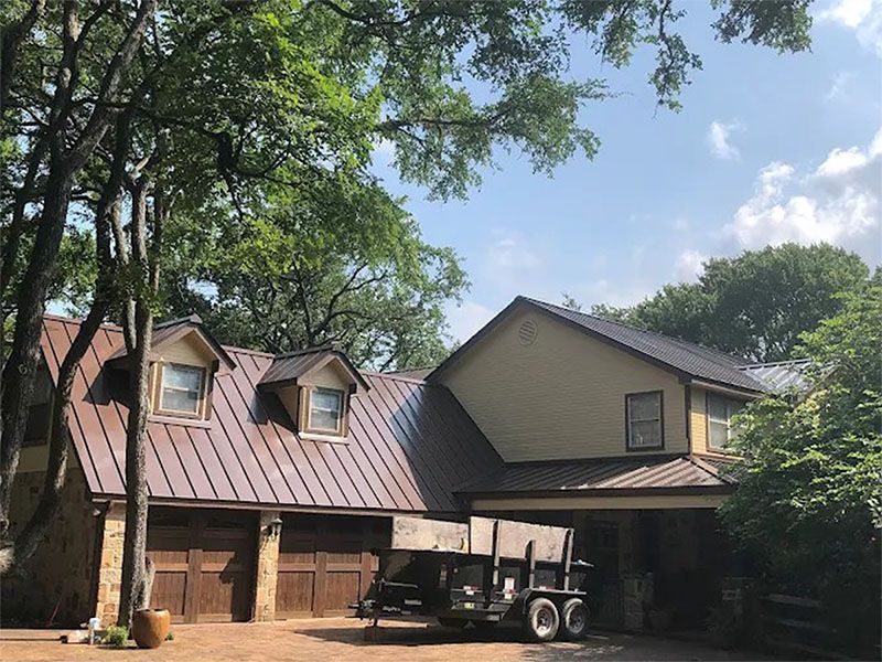 A car is parked in front of a house with a metal roof.