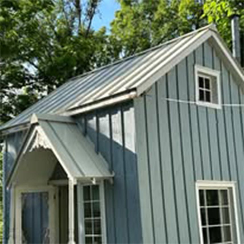 A small blue house with a metal roof and a porch surrounded by trees.