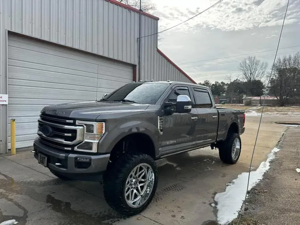 Gray Ford truck with large wheels parked outside a building on a cloudy day.