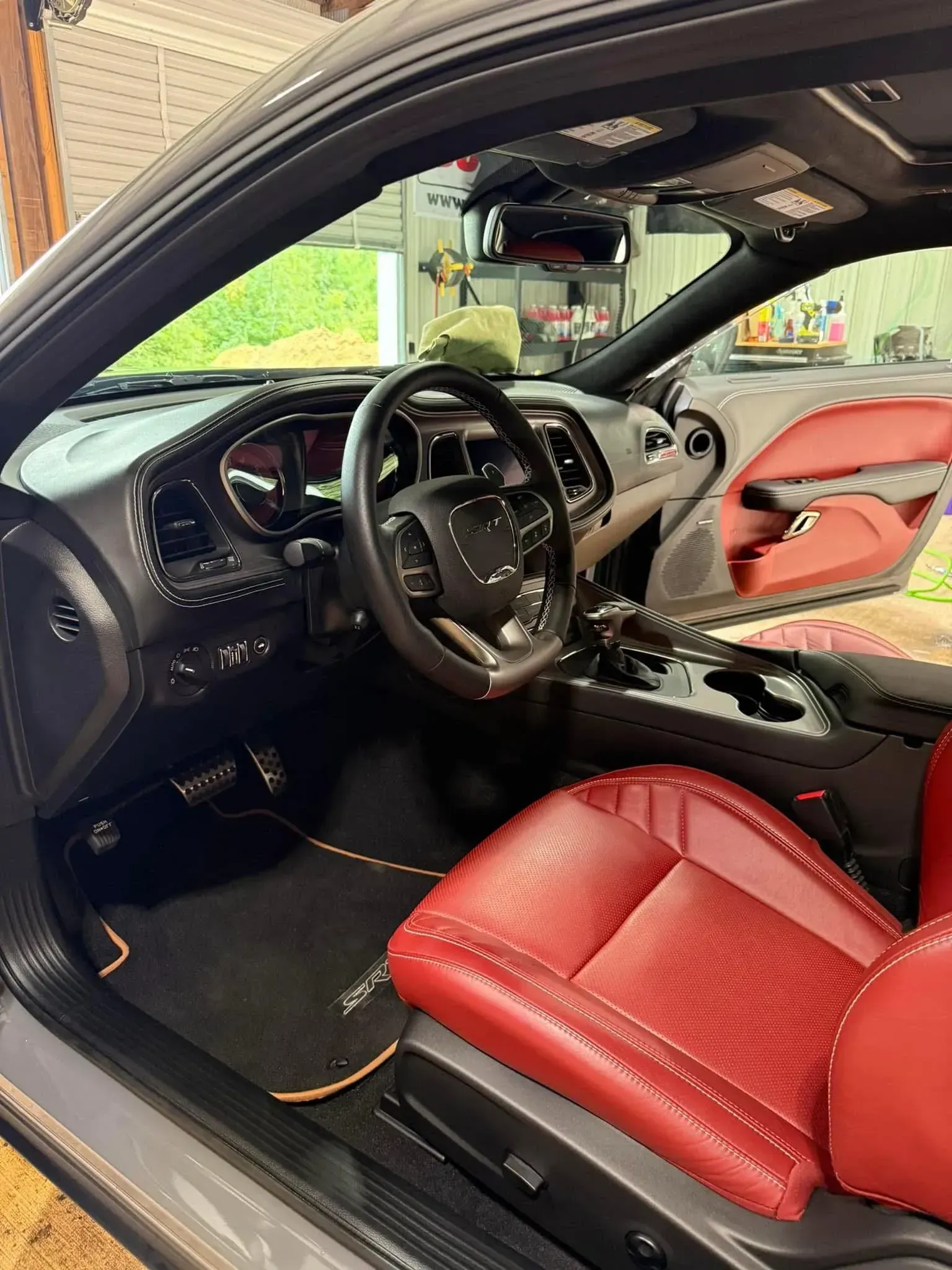 Interior of a red leather Dodge Challenger, with a black steering wheel, in a garage setting.