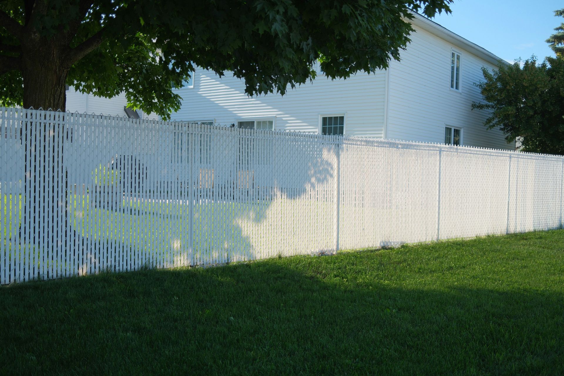A white fence surrounds a lush green yard in front of a white house.
