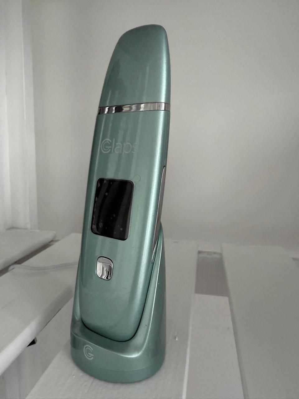 Un aparato de estética verde está sobre una mesa blanca.