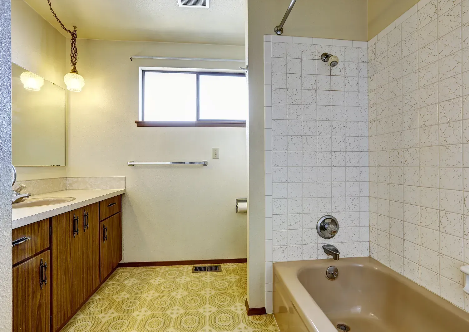 Bathroom with vanity, window, and tub; beige tile and wood cabinets.