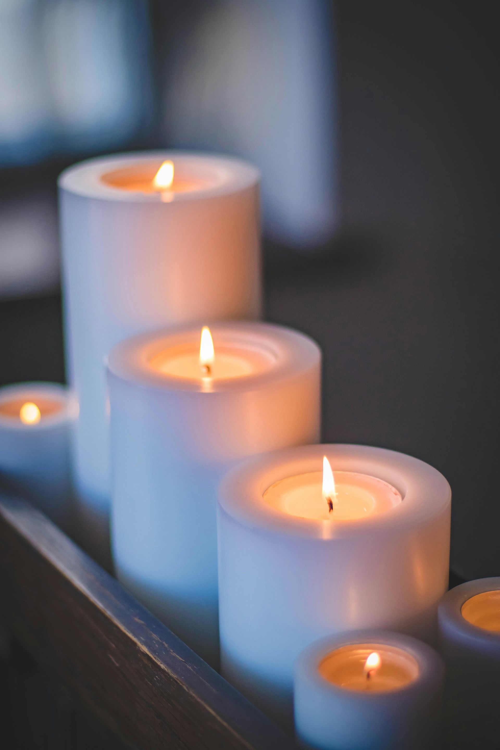Lit white candles on a dark surface, with one small flame glowing in the foreground.