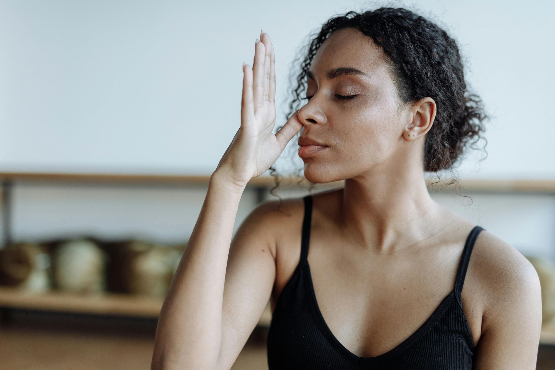Woman in a black sports bra practices breathing with hand raised over her nose in a calm studio setting