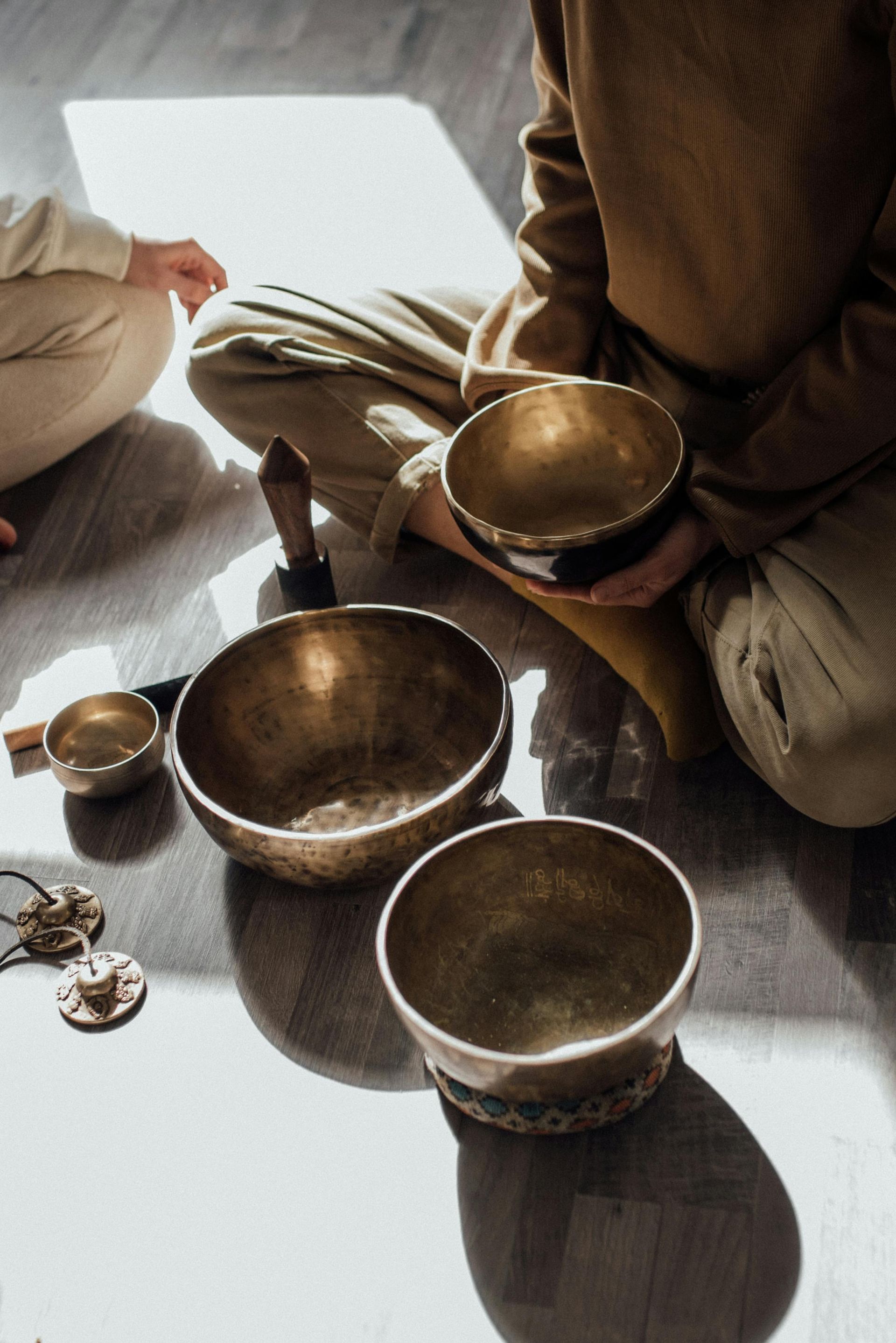 People seated on the floor with singing bowls and a mallet in a calm meditation setting