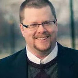 A man wearing glasses and a suit is smiling for the camera.