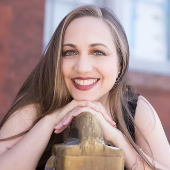 A woman with long hair is smiling with her hands on a statue.