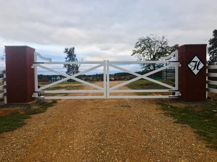 White wooden gate with red brick pillars, gravel driveway, and a cloudy sky.
