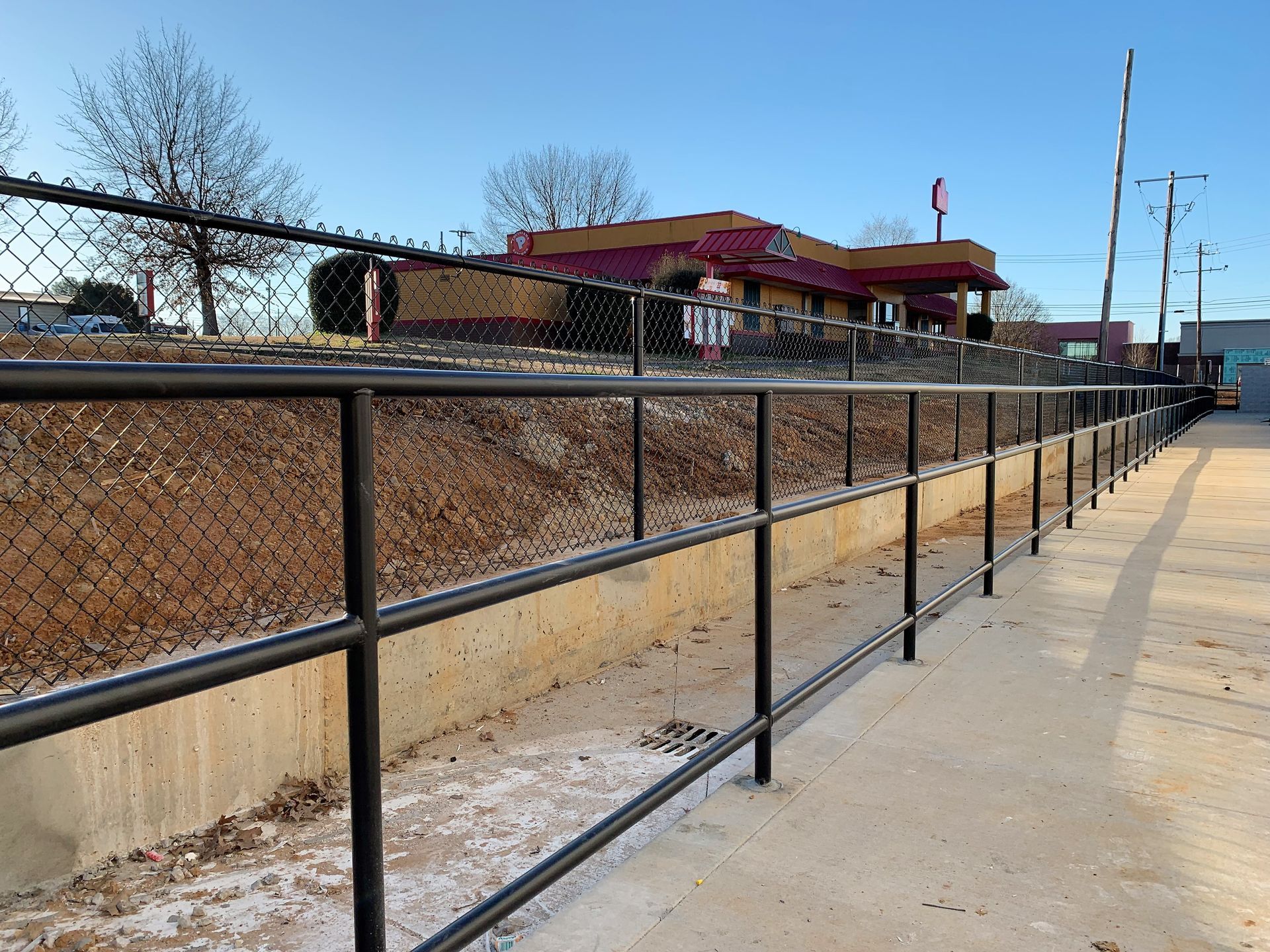 Black handrail and chain link fence alongside a concrete barrier. Restaurant in the background.