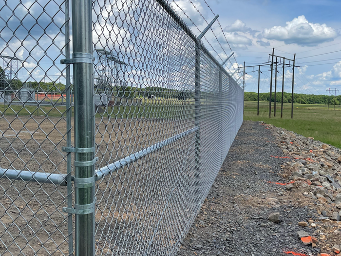 Black metal fence bordering a paved area near beige and brown buildings under a blue sky.
