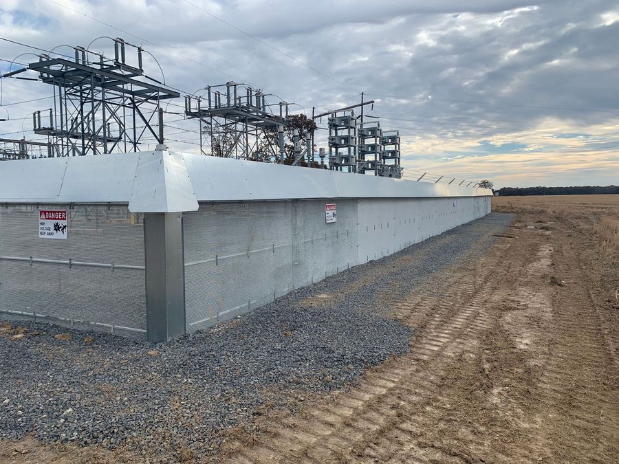 Metal electrical substation building with gravel and dirt ground under cloudy sky.