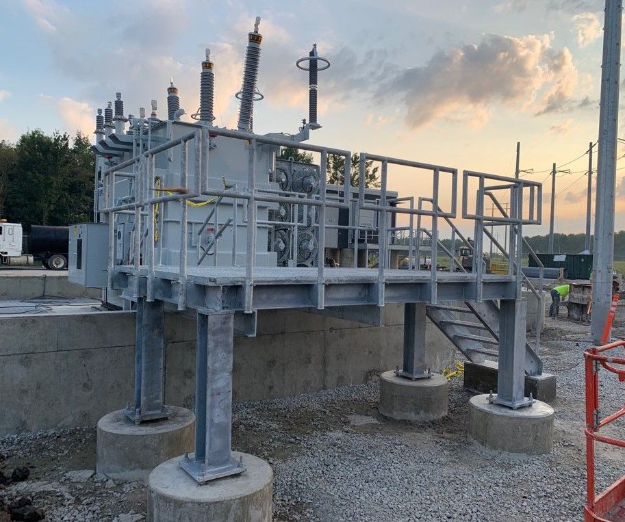 Electrical transformer on a raised platform with metal stairs and handrails, set outdoors.