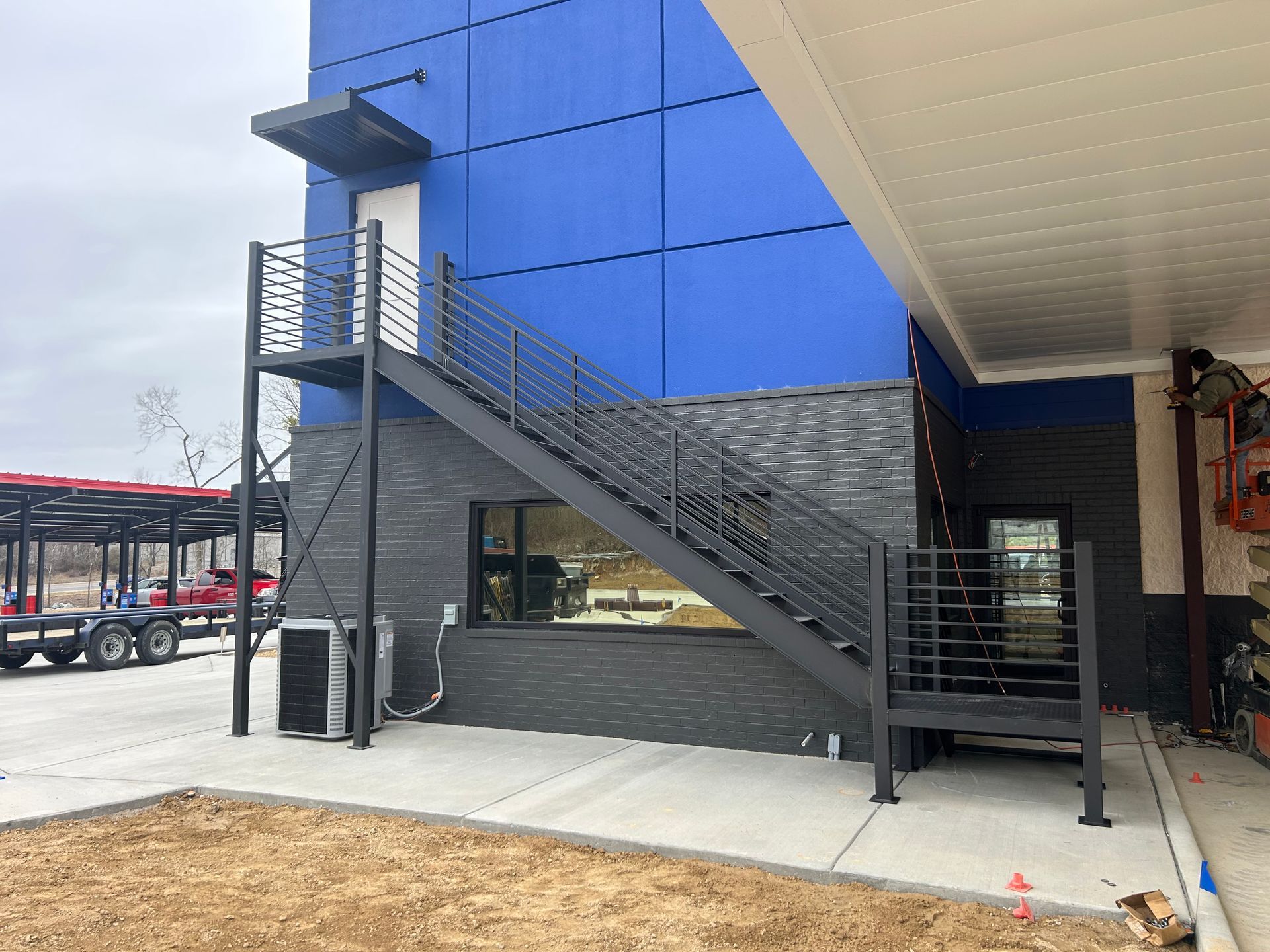 Exterior metal staircase leading to a blue building with a door. Grey brick and a white awning are also visible.