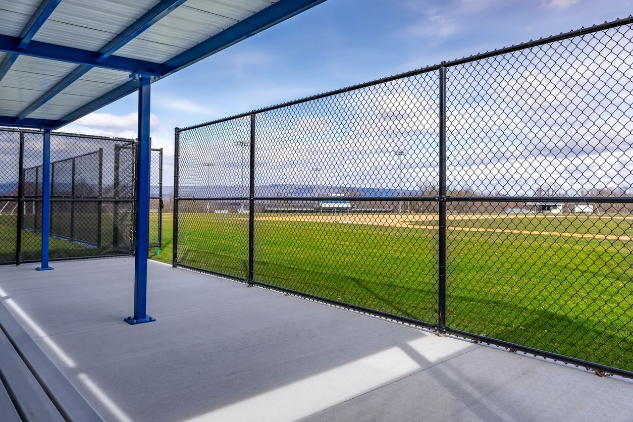 Blue awning and poles over a concrete patio with a chain-link fence bordering a grassy field.