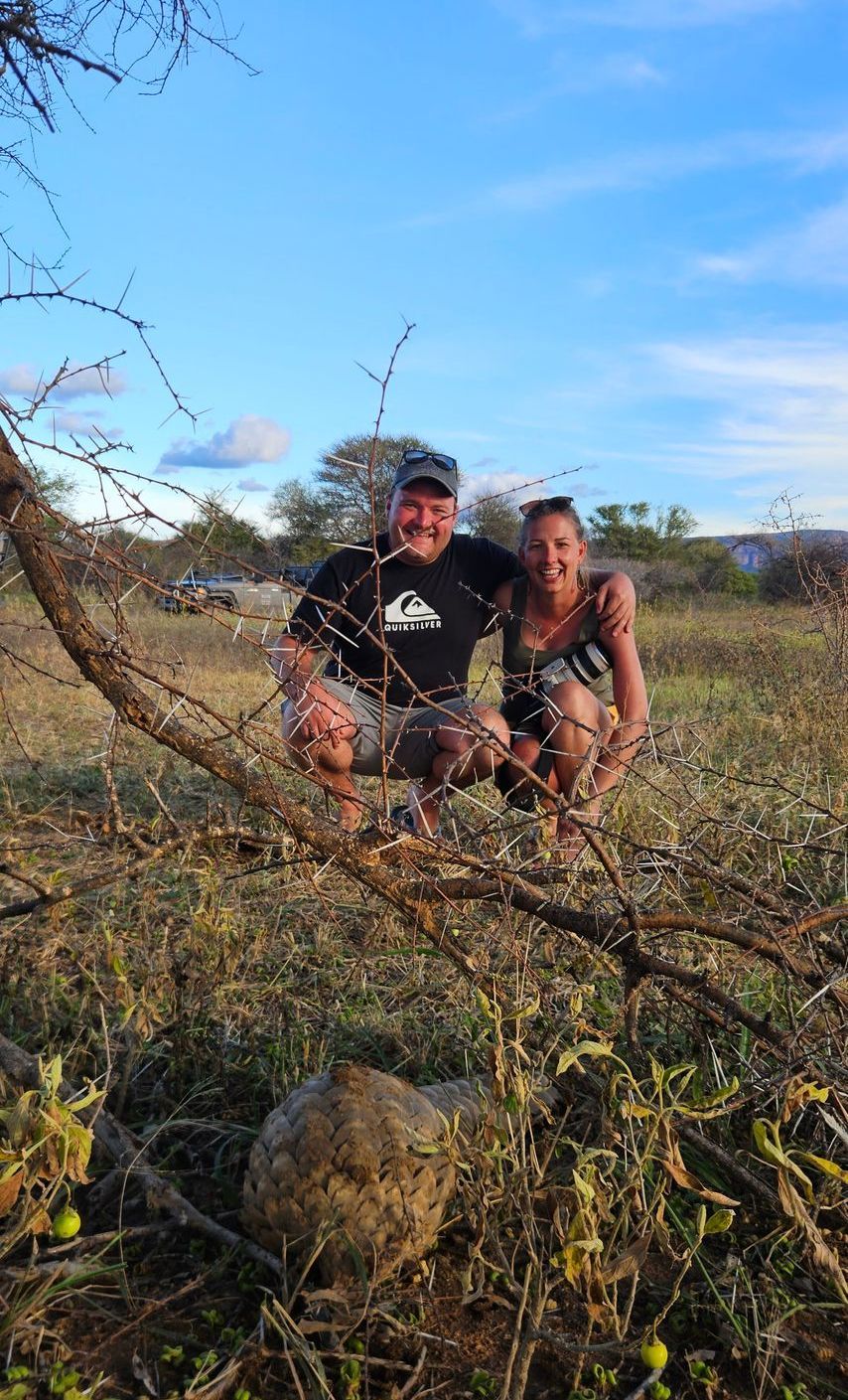 A man and a woman are sitting on a tree branch in a field.