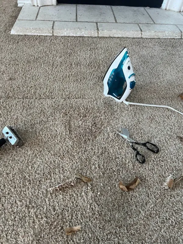 A broken iron is laying on the floor next to a pair of scissors.