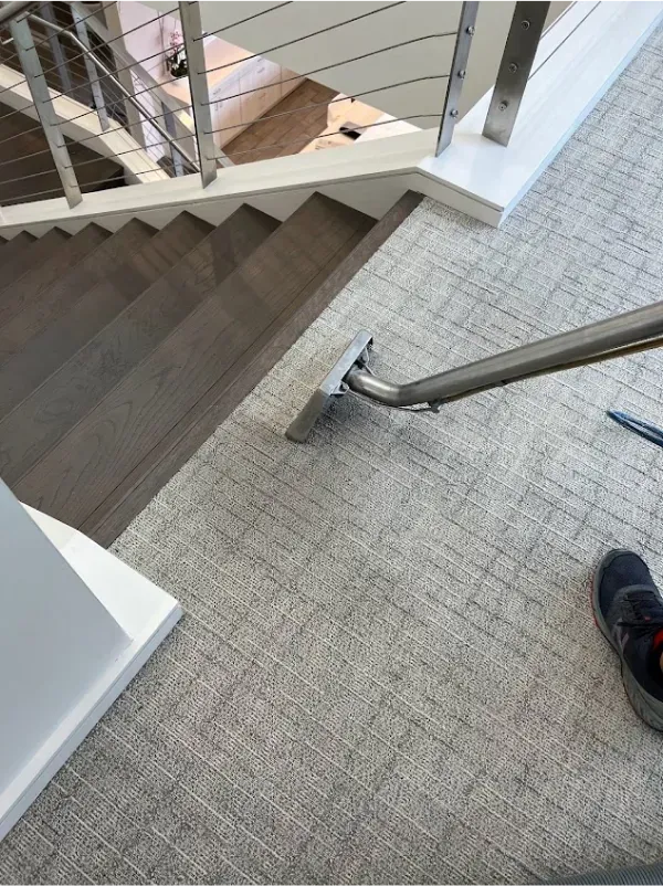 A vacuum cleaner is cleaning a carpeted floor next to a staircase.