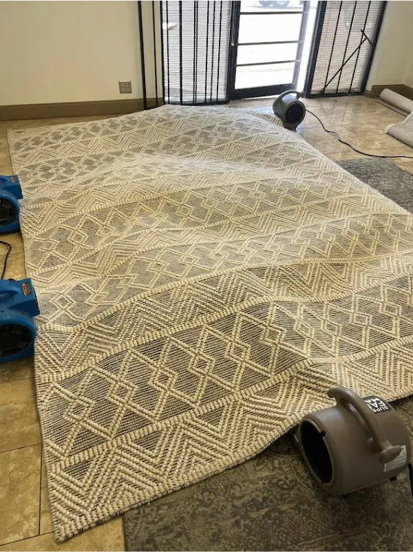 A large rug is sitting on a tiled floor next to a vacuum cleaner.