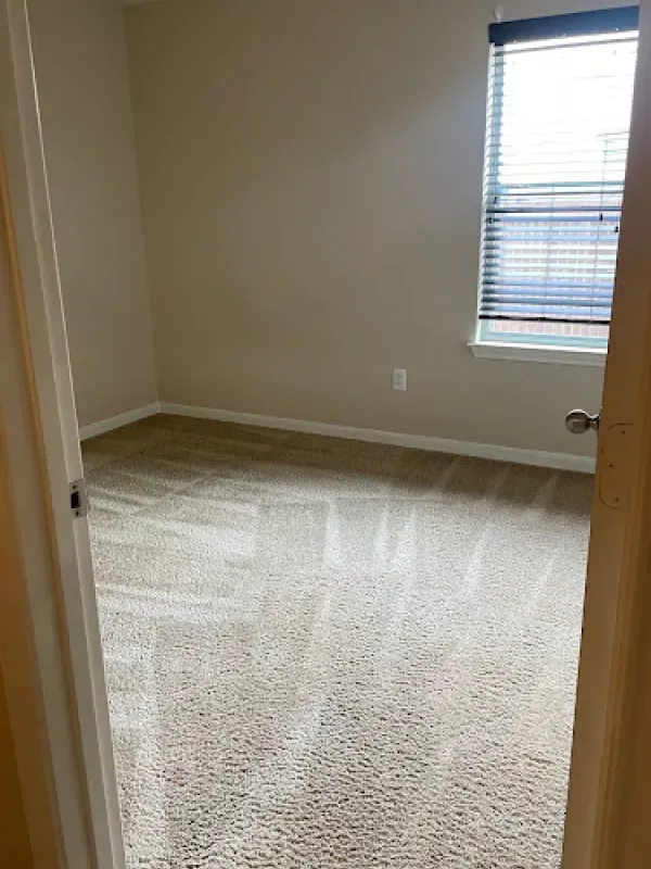 An empty bedroom with a carpeted floor and a window.