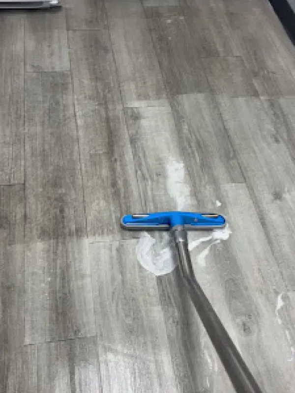 A person is cleaning a wooden floor with a vacuum cleaner.