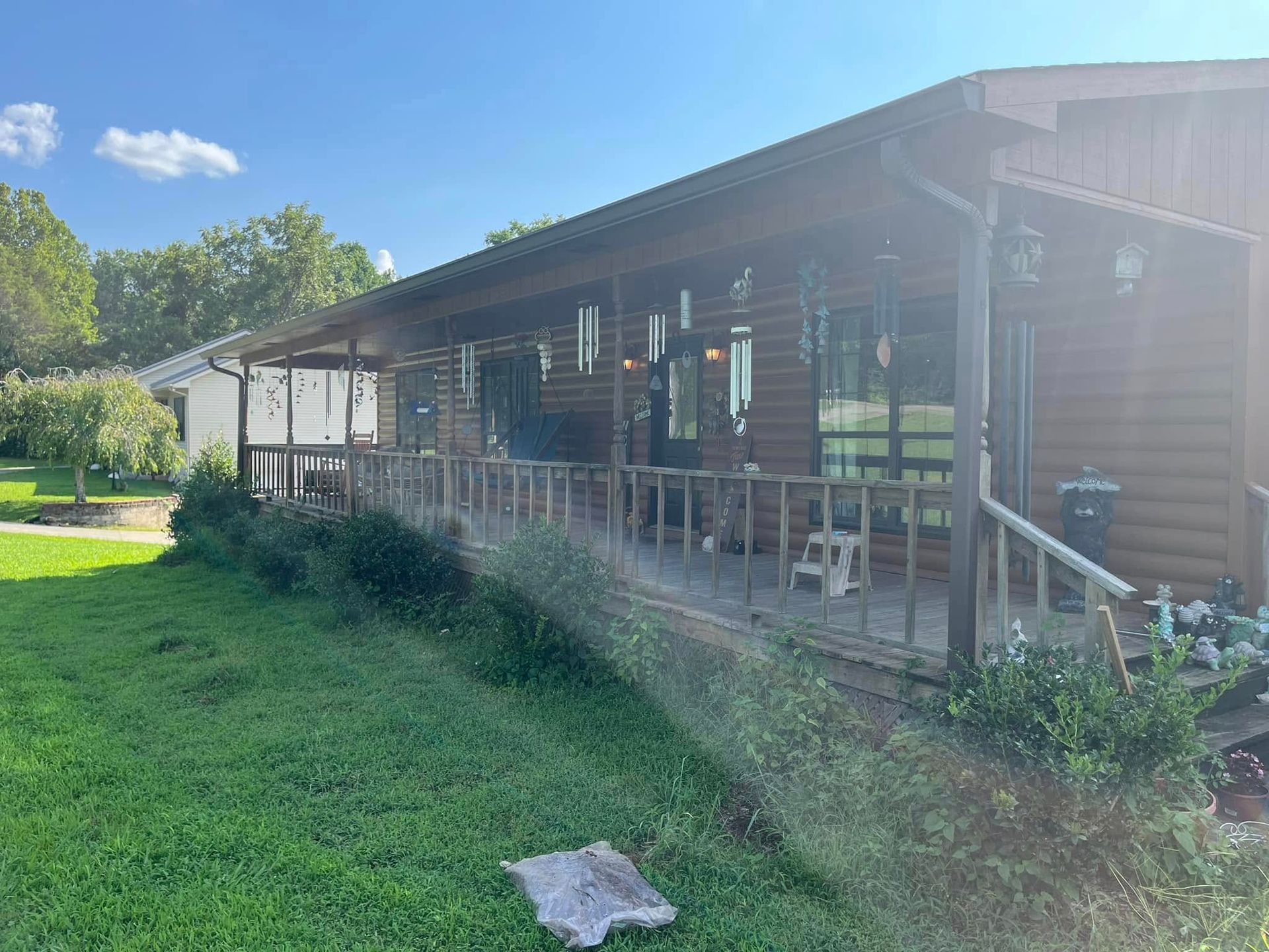 A log cabin with a large porch and stairs is sitting on top of a lush green field.