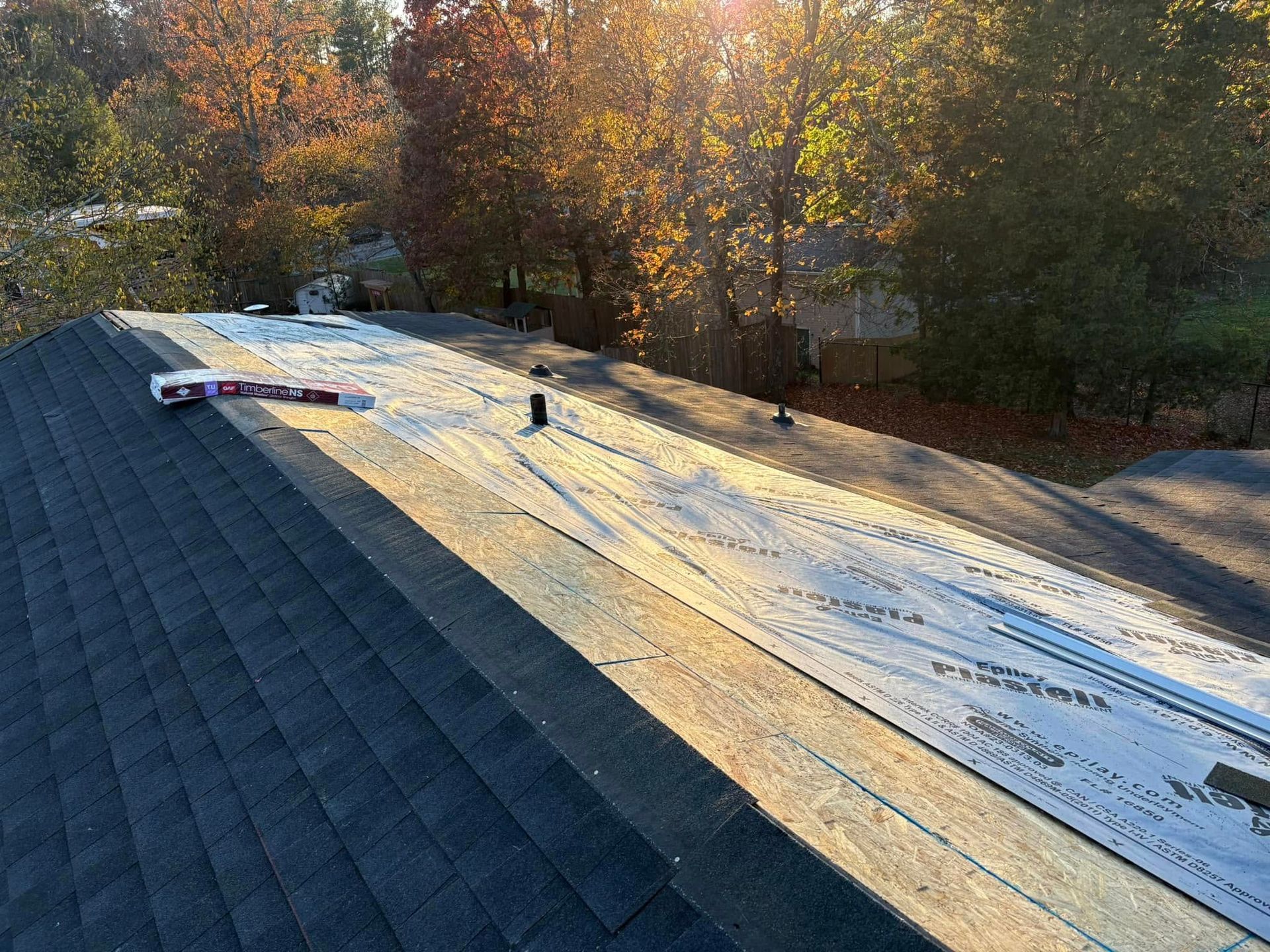 A roof with shingles being installed on it and trees in the background.