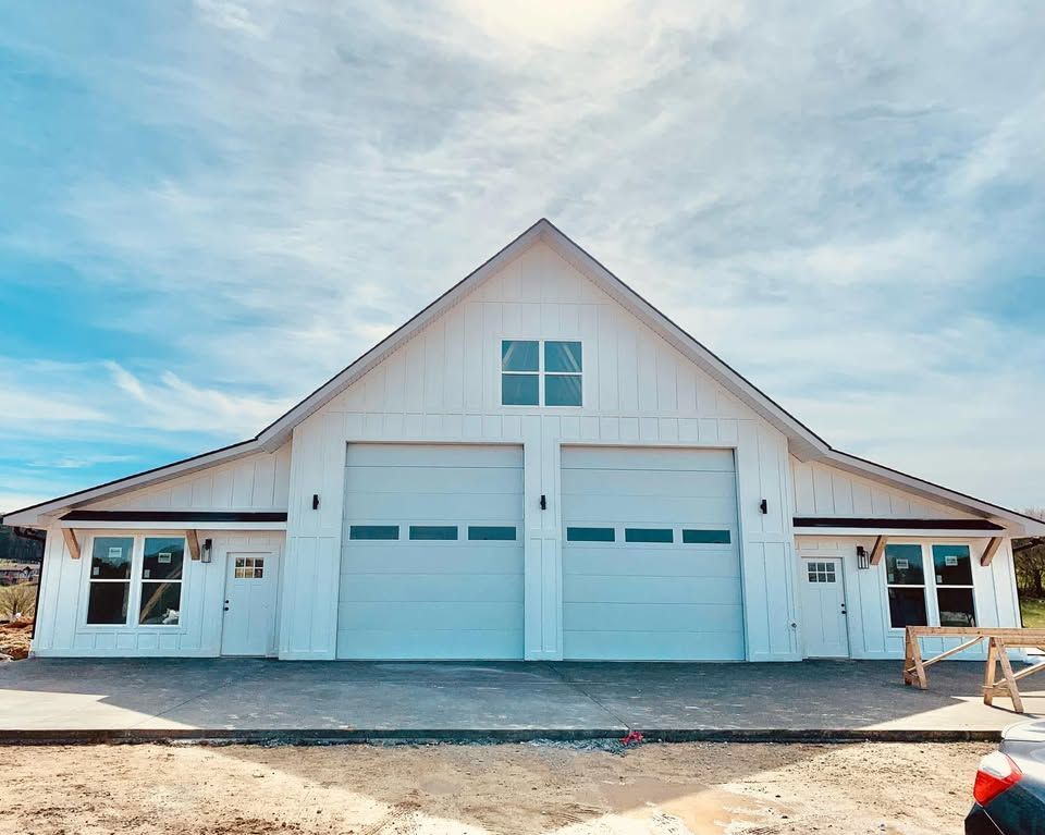 A white barn with two garage doors and a car parked in front of it.