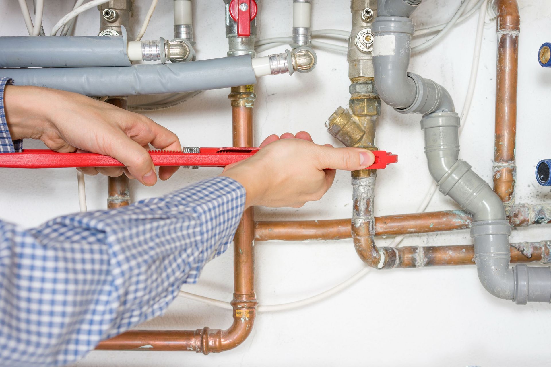Person measuring copper and gray plumbing pipes with a red level under a sink.