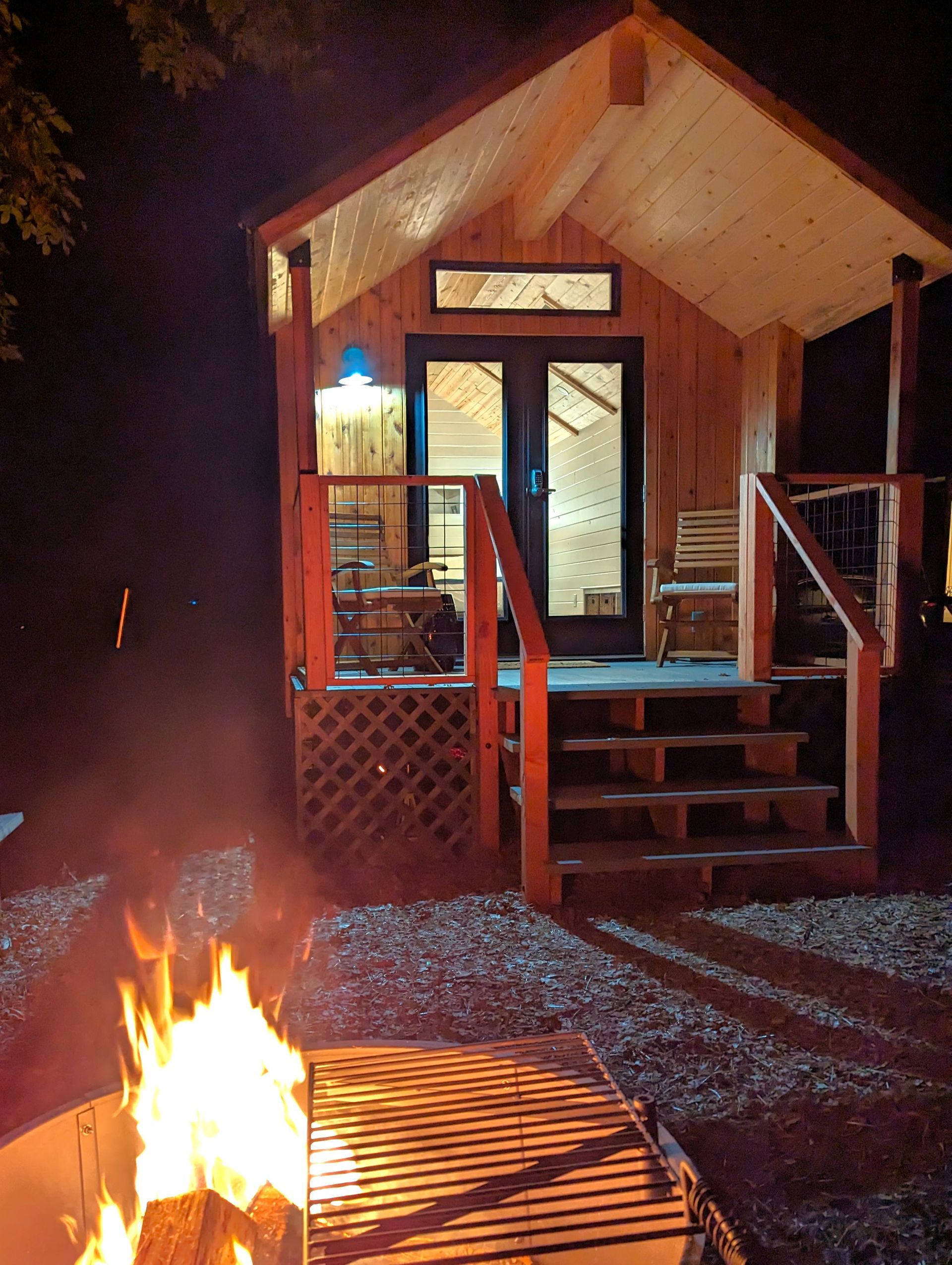 A small cabin with a fire pit in front of it at night.