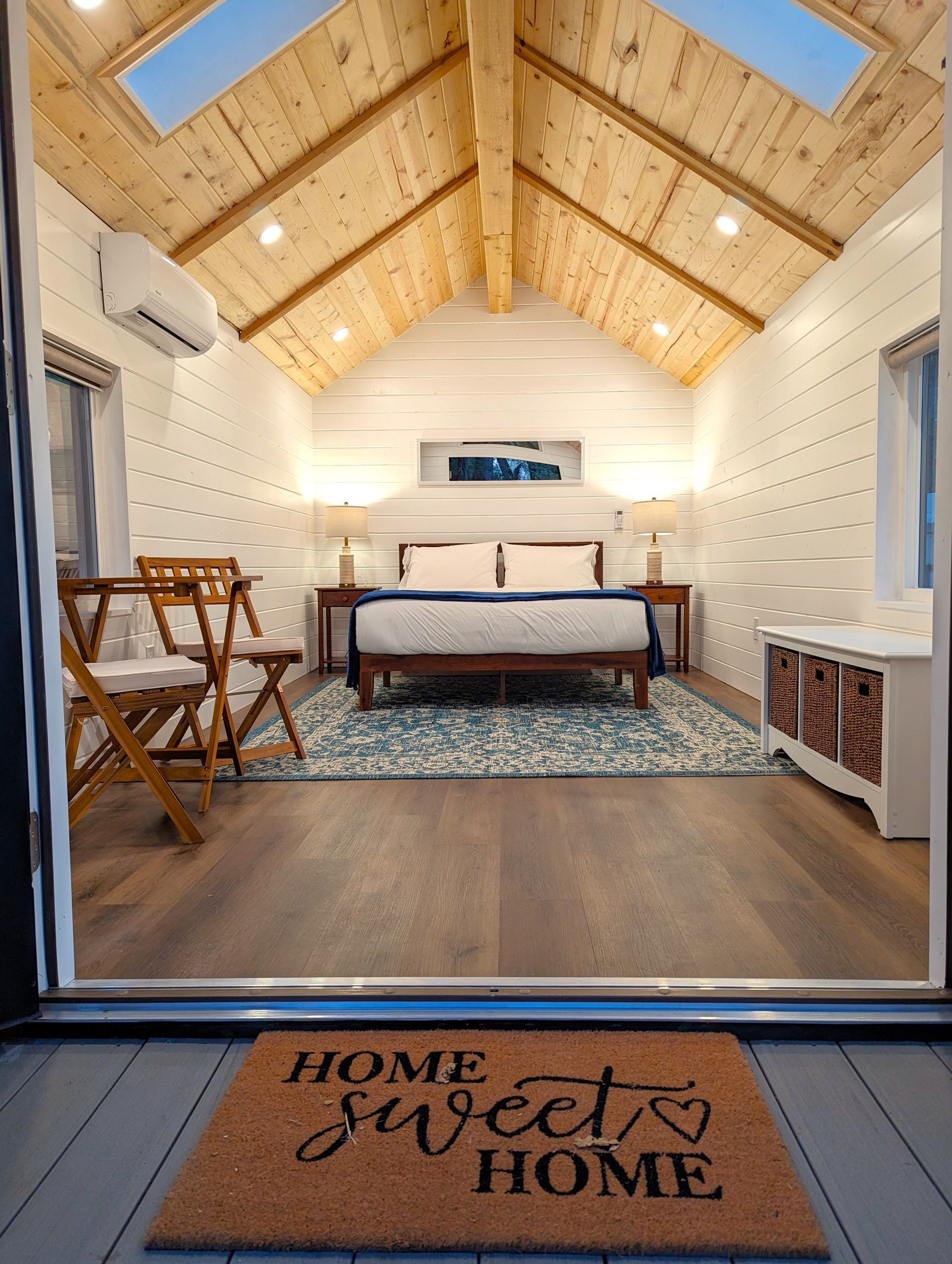 A bedroom with a bed , chairs , and a door mat that says `` home sweet home ''.