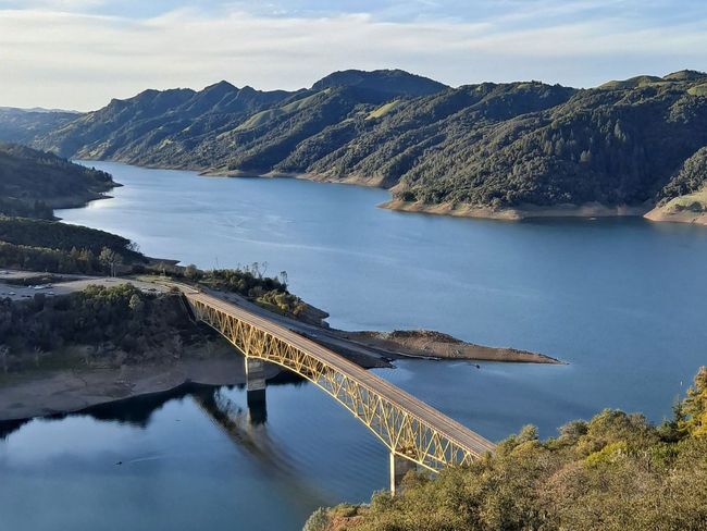 A bridge over a large body of water surrounded by mountains.