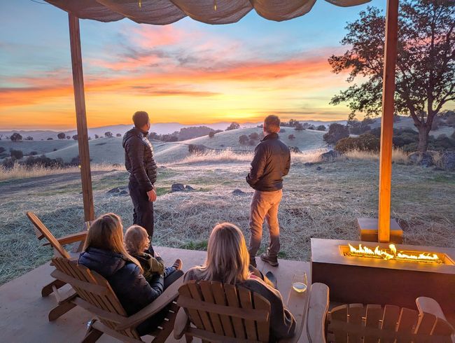 A group of people are sitting on a porch looking at the sunset.