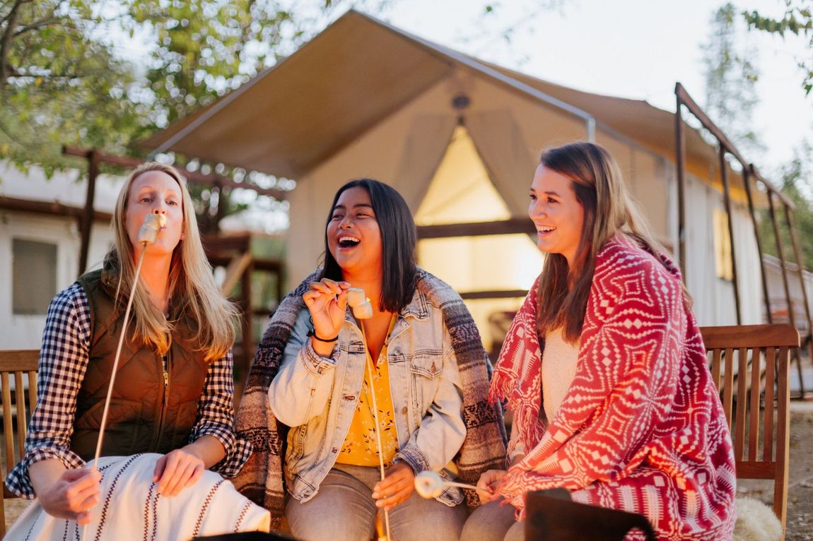 Three women are sitting around a campfire eating marshmallows.