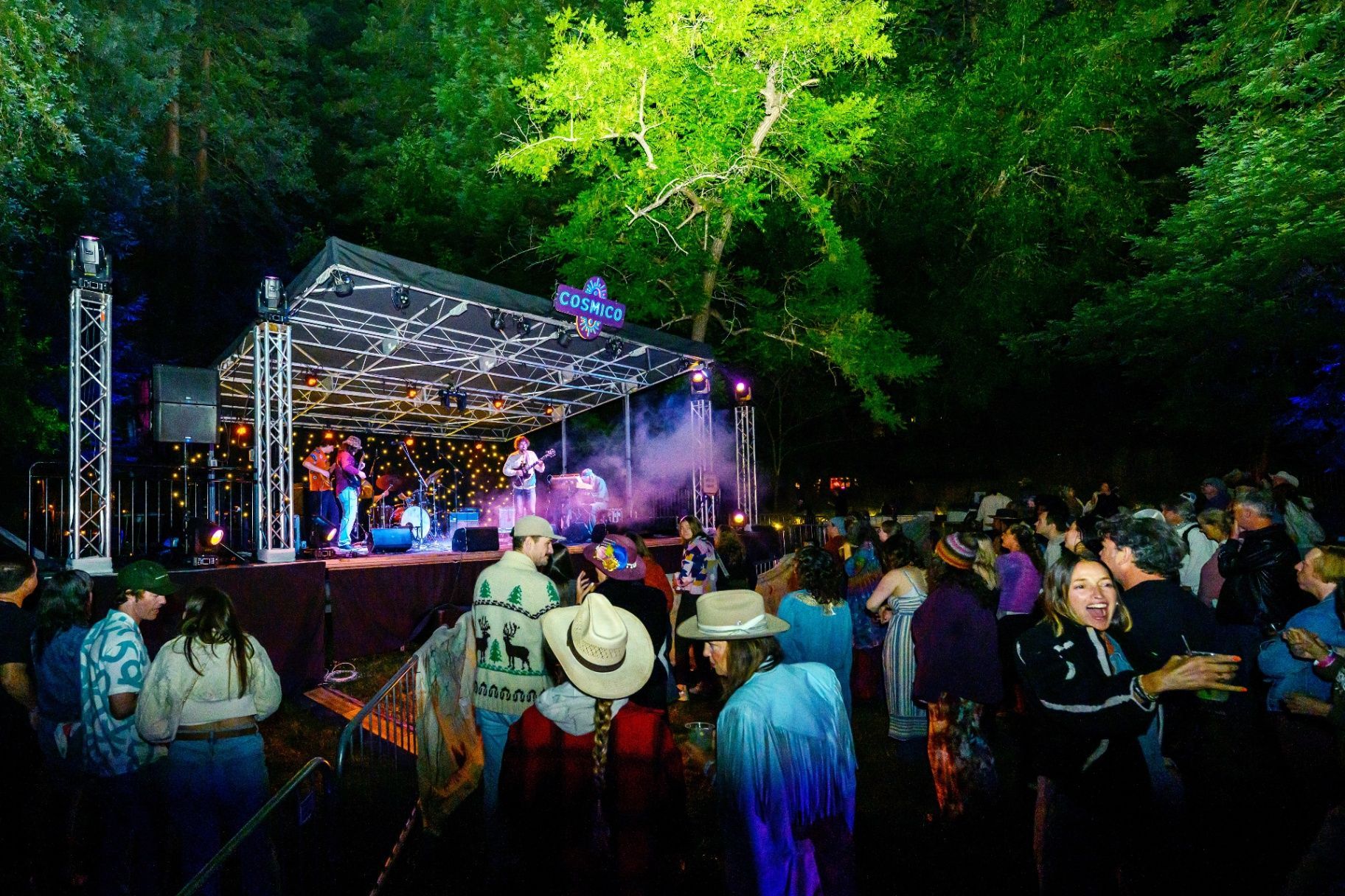 A woman in a hat is standing in front of a tent with her arms in the air.