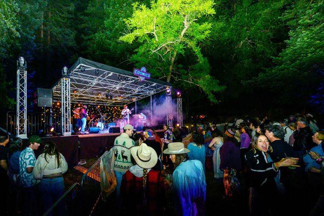 A woman in a hat is standing in front of a tent with her arms in the air.
