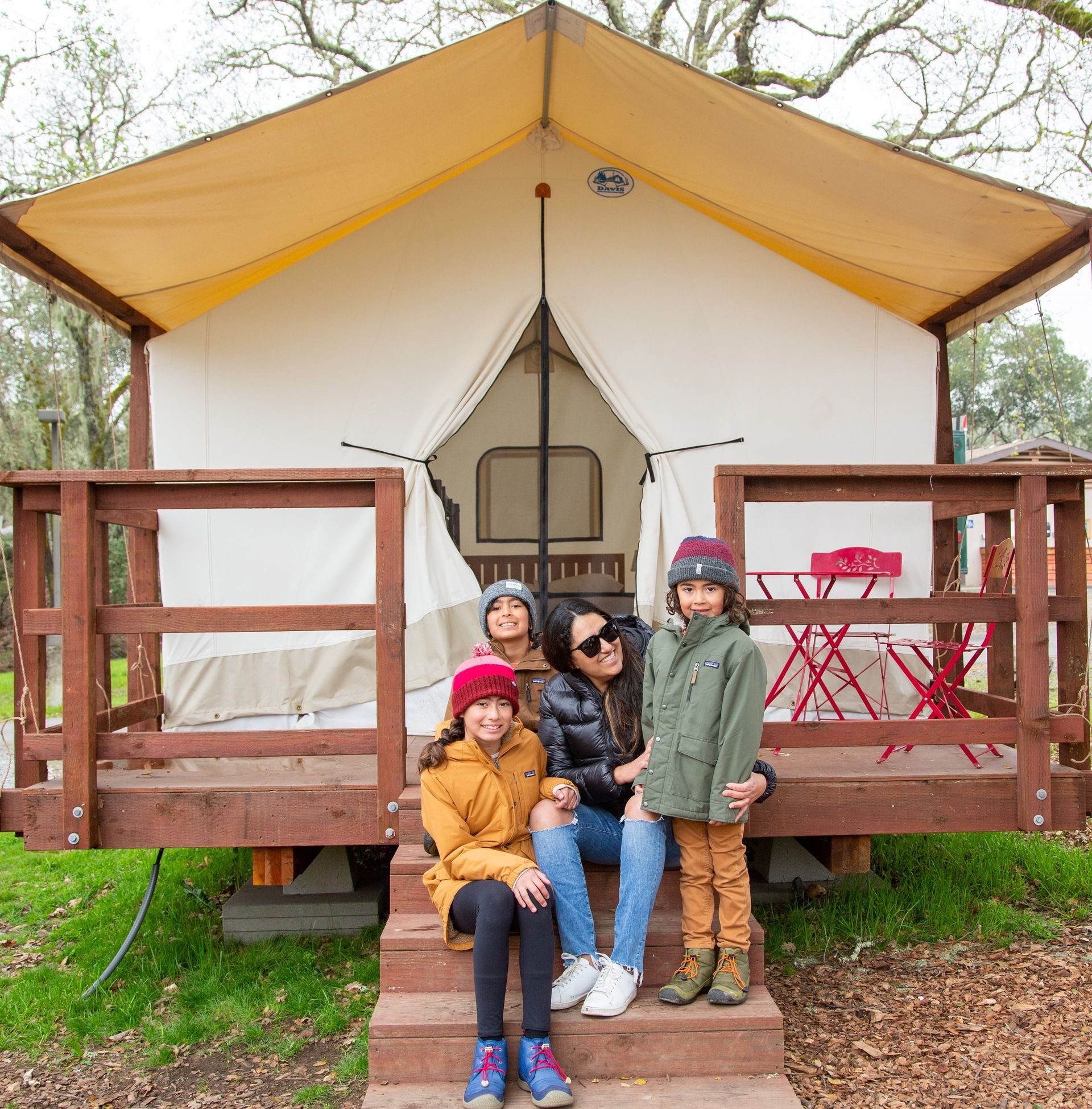 A family is sitting on the steps of a tent.