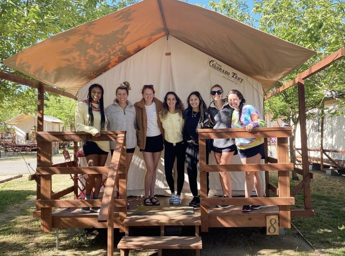 A group of young women are posing for a picture in front of a tent.