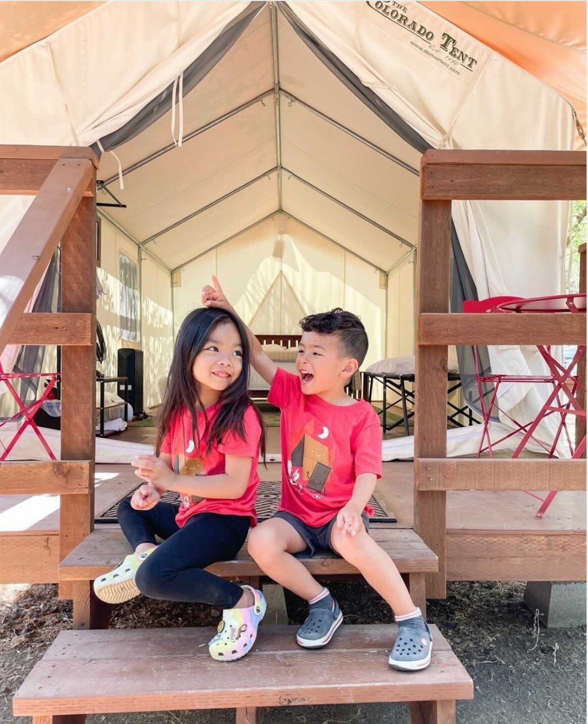 A boy and a girl are sitting on steps in front of a tent.