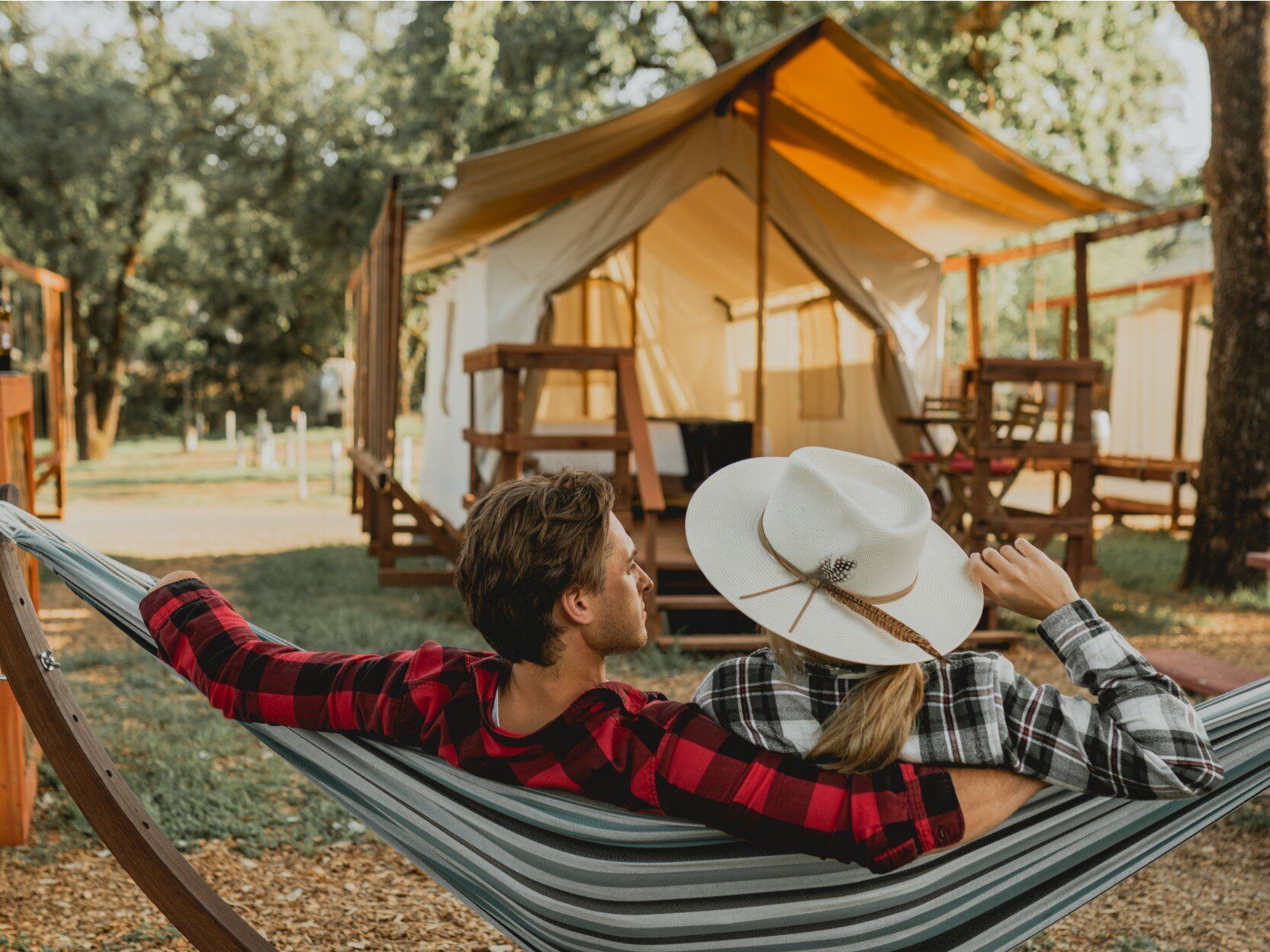 A man and a woman are laying in a hammock in front of a tent.