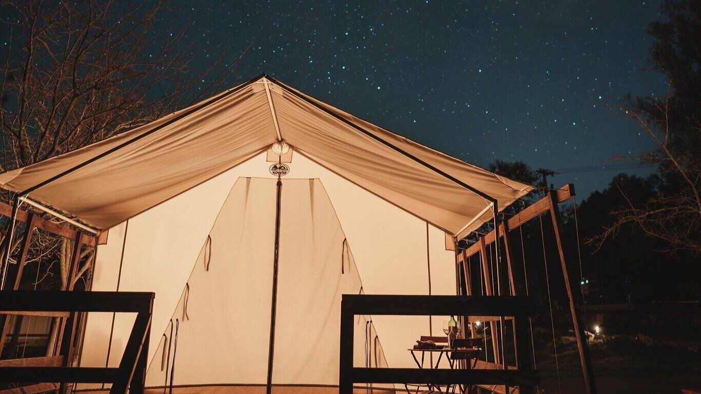 A tent is lit up at night under a starry sky.