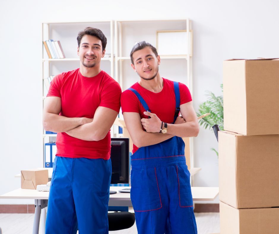 Two men are standing next to each other in front of a pile of cardboard boxes.