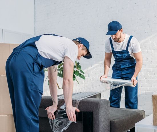 Two men are wrapping a couch with plastic wrap.