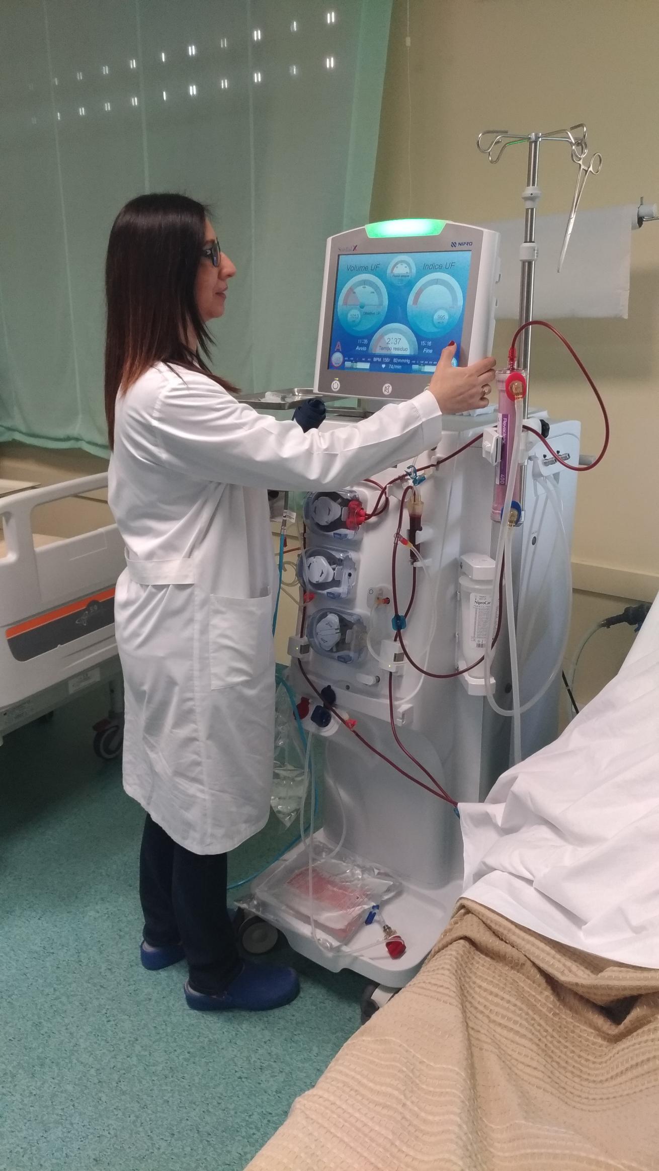 Una donna in camice da laboratorio sta lavorando a una macchina in una stanza d'ospedale.