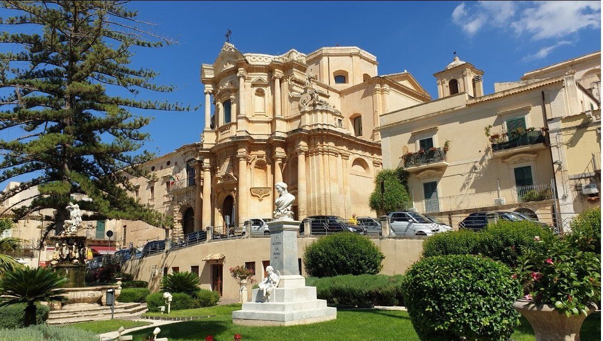 Un grande edificio con una fontana di fronte è circondato da alberi e cespugli.