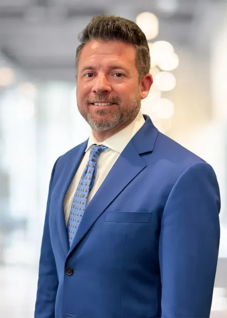 Man in blue suit and tie smiling, posed in a bright office setting.
